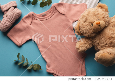 Flat lay of pink baby grow, hat, teddy bear and pink booties with copy space on blue background 105942724