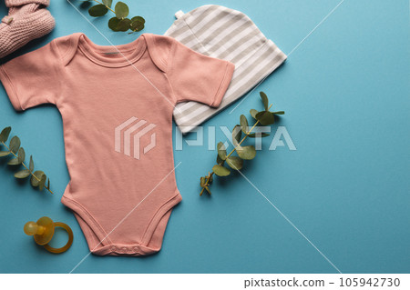Flat lay of pink baby grow, hat, dummy and pink booties with copy space on blue background Flat lay of pink baby grow, hat, dummy and pink booties with copy space on blue background 105942730