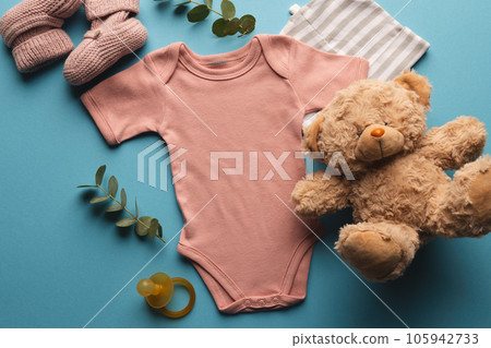 Flat lay of pink baby grow, hat, teddy bear and pink booties with copy space on blue background Flat lay of pink baby grow, hat, teddy bear and pink booties with copy space on blue background 105942733