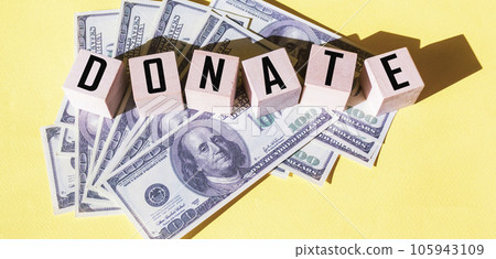 DONATE text on wooden cubes. Dollars lie on a yellow background DONATE text on wooden cubes. Dollars lie on a yellow background 105943109
