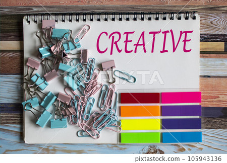 The text on the notebook is Creative. Nearby are paper clips, colored stickers. The text on the notebook is Creative. Nearby are paper clips, colored stickers. 105943136