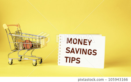 MONEY SAVING TIPS text on notepad, next to a small cart with coins on a yellow background. Business and concept 105943166