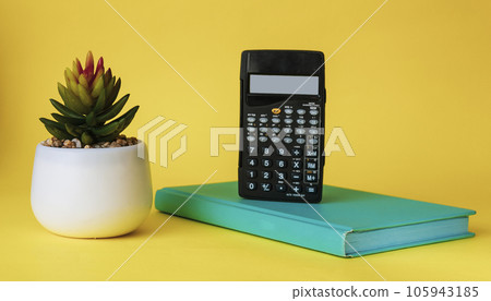 Calculator on a green notebook with a cactus flower on a yellow background. 105943185
