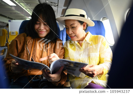 Smiling middle aged woman and daughter reading reading magazines in passenger airplane, waiting for airplane landing Smiling middle aged woman and daughter reading reading magazines in passenger airplane, waiting for airplane landing 105943237