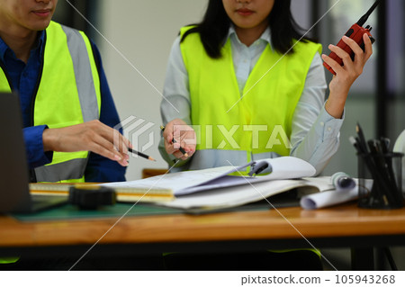 Architects man and woman working on blueprint and discussing the new project in office. 105943268