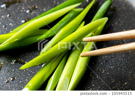 A cooking scene where garlic sprouts (diagonally cut) are fried in a frying pan. 105943515