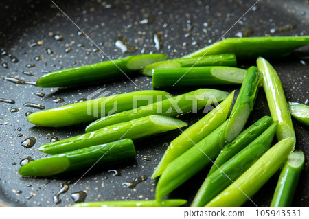 A cooking scene where garlic sprouts (diagonally cut) are fried in a frying pan. 105943531