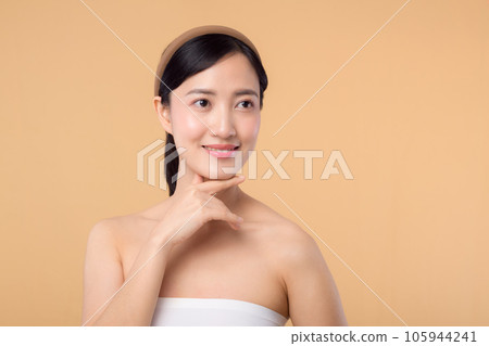 Beautiful girl asian model touching fresh glowing hydrated facial skin on beige background closeup. Beauty face young woman with natural makeup and healthy skin portrait. Skin care concept 105944241