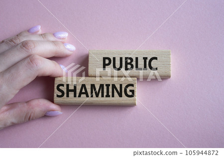 Public Shaming symbol. Concept word Public Shaming on wooden blocks. Businessman hand. Beautiful pink background. Business and Public Shaming concept. Copy space 105944872