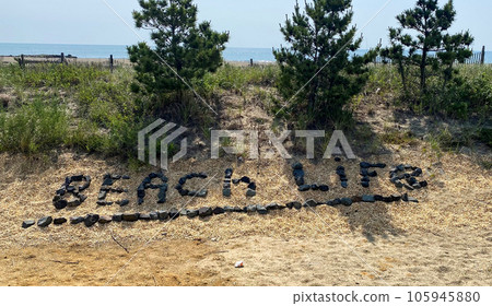 Beach life spelled out with small black rocks on a sand dune 105945880