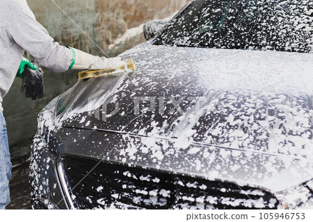 Male worker washing car at car station outdoors with foam and yellow sponge. Male worker washing car at car station outdoors with foam and yellow sponge. 105946753