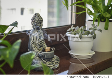 Candlestick in the shape of a buddha, smoldering Palo Santo and houseplants Candlestick in the shape of a buddha, smoldering Palo Santo and houseplants 105947621