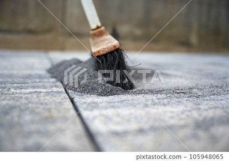 Broom pushing a tile gaps sand in between concrete tiles for outdoor patio 105948065