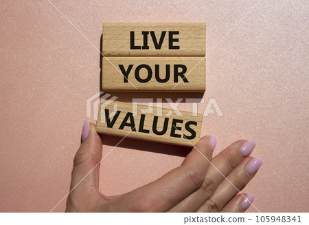 Live your values symbol. Concept words 'Live your values' on wooden blocks. Beautiful pink background. Businessman hand. Business and Live your values concept. Copy space. Live your values symbol. Concept words 'Live your values' on wooden blocks. Beautiful pink background. Businessman hand. Business and Live your values concept. Copy space. 105948341