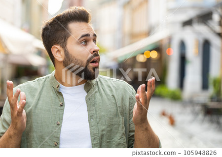 Young man looking surprised at camera shocked by sudden win good victory news, wow in city street 105948826