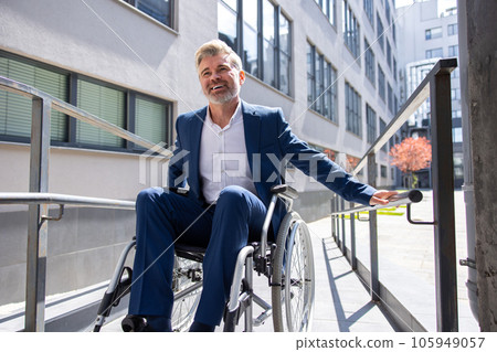 Gray haired businessman in formal wear gets to work in wheelchair rides ramp. 105949057