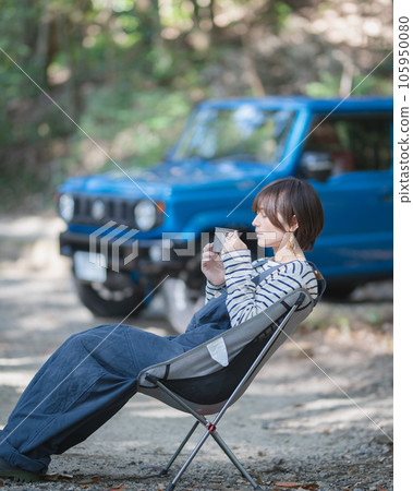 A woman sitting on an outdoor chair and drinking a drink with a blue car in the background 105950080