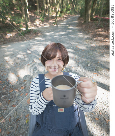 A woman sitting on a chair at a campsite and offering a drink A woman sitting on a chair at a campsite and offering a drink 105950083
