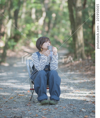 A woman sitting on a chair at a campsite and drinking a drink alone 105950085