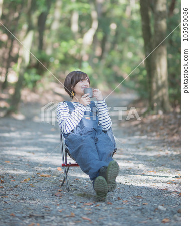 A woman sitting on a chair at a campsite and drinking a drink alone A woman sitting on a chair at a campsite and drinking a drink alone 105950086