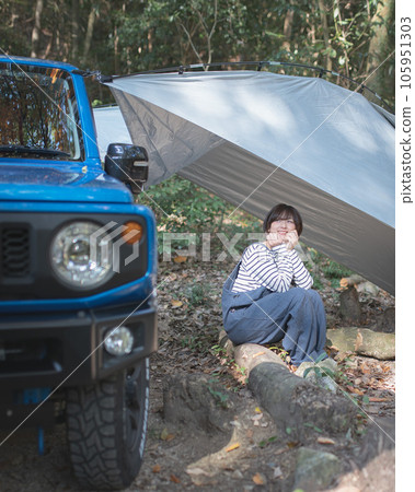 A woman in overalls looking at her car at a campsite 105951303