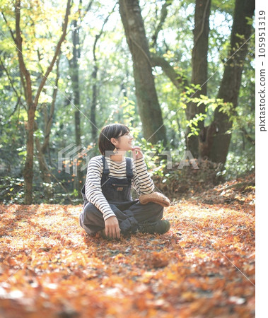 Outdoor girl sitting in fallen leaves and looking sideways with a smile 105951319