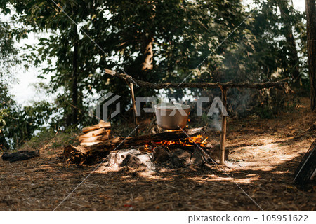 Travel a kettle over a fire burning on the river and sunset backgroun. Cooking over a campfire Travel a kettle over a fire burning on the river and sunset backgroun. Cooking over a campfire 105951622