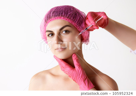 Young woman doing cosmetological injection on face against white studio background Young woman doing cosmetological injection on face against white studio background 105952324