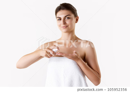 Beautiful young brunette woman applying face cream, taking care after skin condition against white studio background Beautiful young brunette woman applying face cream, taking care after skin condition against white studio background 105952356