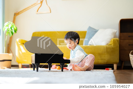 一個 3 歲的男孩在客廳裡彈玩具鋼琴 105954027