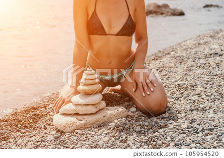 Woman bilds stones pyramid on seashore on a sunny day on the blue sea background. Happy holidays. Pebble beach, calm sea, travel destination. Concept of happy vacation on the sea, meditation, spa. Woman bilds stones pyramid on seashore on a sunny day on the blue sea background. Happy holidays. Pebble beach, calm sea, travel destination. Concept of happy vacation on the sea, meditation, spa. 105954520