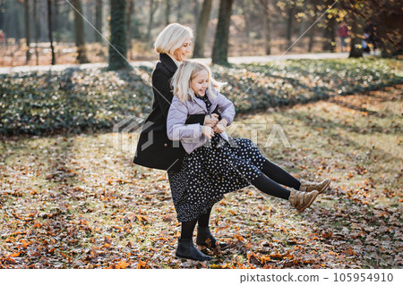 Carefree mother spinning her teenager daughter in autumn day on city public park. Mother and teen daughter playing together in fall park 105954910
