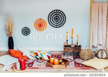 Decorated cozy autumn interior for relax during fall holidays. Comfy floor location with cushions, wicker pumpkins, burning candles. Thanksgiving, Halloween plans at home. Romantic date, movie night 105954924