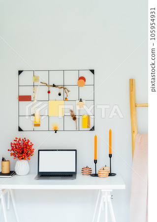 Home office desk with open laptop mockup, grid mood board with fall colors palette and seasonal decor like candles, flowers, pumpkins. Autumn inspiration and cozy mood. Hygge home fall decor. Vertical 105954931