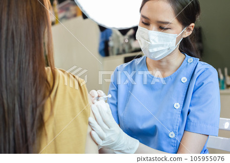 Female doctor wearing mask holding syringe giving vaccinations to patient for protection. Female doctor wearing mask holding syringe giving vaccinations to patient for protection. 105955076