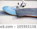 Applying grip tape to a brand new skateboard deck next to a set of trucks and wheels 105955138