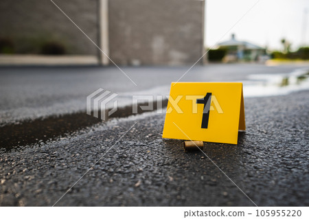 One yellow crime scene evidence marker on the street after a gun shooting brass bullet shell casing 9mm handgun pistol One yellow crime scene evidence marker on the street after a gun shooting brass bullet shell casing 9mm handgun pistol 105955220