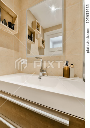 a modern bathroom with beige tile walls and white counters, along with a large mirror above the sink area 105955683