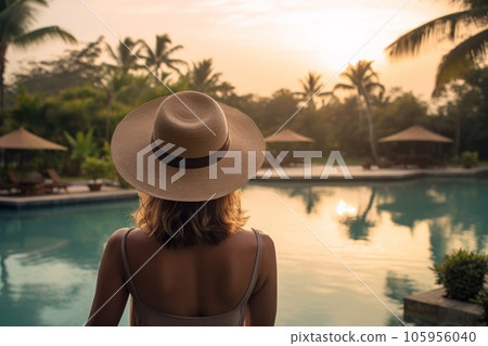 A woman wearing a hat looking at the water of a lagoon hotel and a swimming pool A woman wearing a hat looking at the water of a lagoon hotel and a swimming pool 105956040