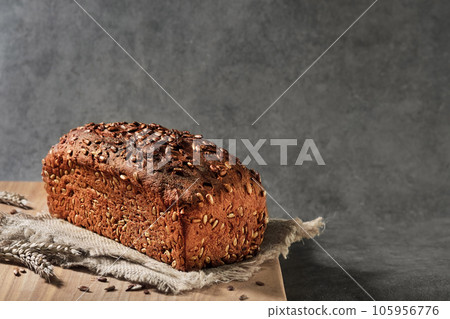 Delicious and healthy wheat - rye bread with seeds on sacking, close-up with selective focus. Fermented wholesome bread, healthy food. Loaf on gray background with space for text 105956776