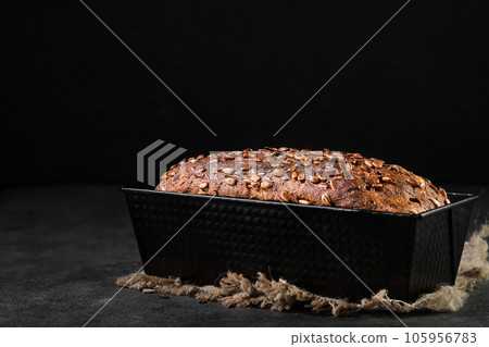 Homemade freshly baked wheat rye bread with seeds in a baking dish, close-up with selective focus. Freshly baked fermented bread cools down after baking, dark background with space for text 105956783