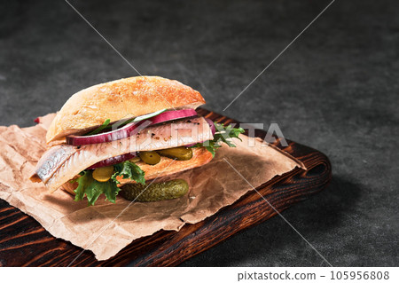 Dutch sandwich with herring and pickles cucumber and red onion on the gray table. Close up, selective focus and copy space Dutch sandwich with herring and pickles cucumber and red onion on the gray table. Close up, selective focus and copy space 105956808