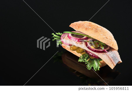 Traditional Dutch sandwich with herring and pickles cucumber and red onion on the dark mirror table. Close up, selective focus and copy space Traditional Dutch sandwich with herring and pickles cucumber and red onion on the dark mirror table. Close up, selective focus and copy space 105956811
