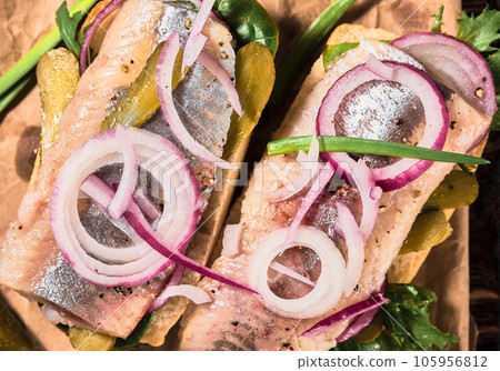 Open sandwich with bread, pickled herring, pickled cucumber and red onion on a paper lining. Danish smorebrod, selective focus and copy space Open sandwich with bread, pickled herring, pickled cucumber and red onion on a paper lining. Danish smorebrod, selective focus and copy space 105956812