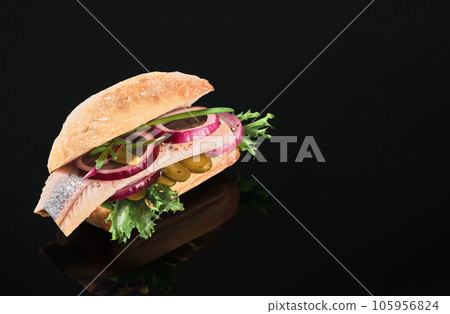 Dutch sandwich with herring and pickles pickled cucumber and red onion on the dark mirror table. Close up, selective focus and copy space Dutch sandwich with herring and pickles pickled cucumber and red onion on the dark mirror table. Close up, selective focus and copy space 105956824