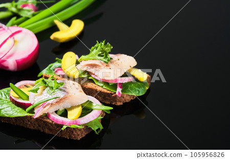 Open sandwich with dark rye bread, marinated matias herring, pickled cucumber and red onion on tha dark mirror table. Danish smorrebrod, selective focus and copy space 105956826