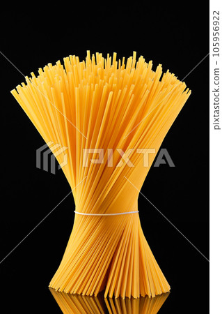 Raw spaghetti tied in a sheaf stands on a dark glass on a black background. whole grain italian spaghetti pasta 105956922
