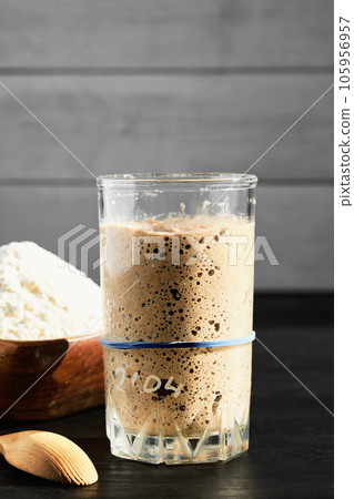 Rye and wheat sourdough starter in glass jar, with ingredient - flour. Close up, selective focus in the glass, vertical frame 105956957