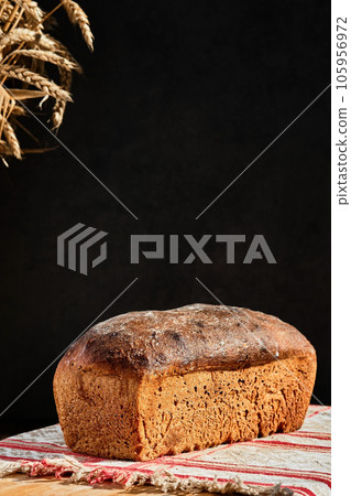 Freshly baked artisan whole grain bread from rye and wheat sourdough, on rustic gray kitchen towel, dark background. Vertical shot, selective focus on a loaf of bread 105956972