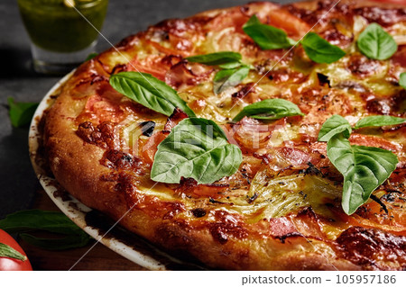 Italian pizza with ham, mozzarella, tomatoes and basil leaves on a dark background. Close-up with selective focus on homemade pizza. 105957186